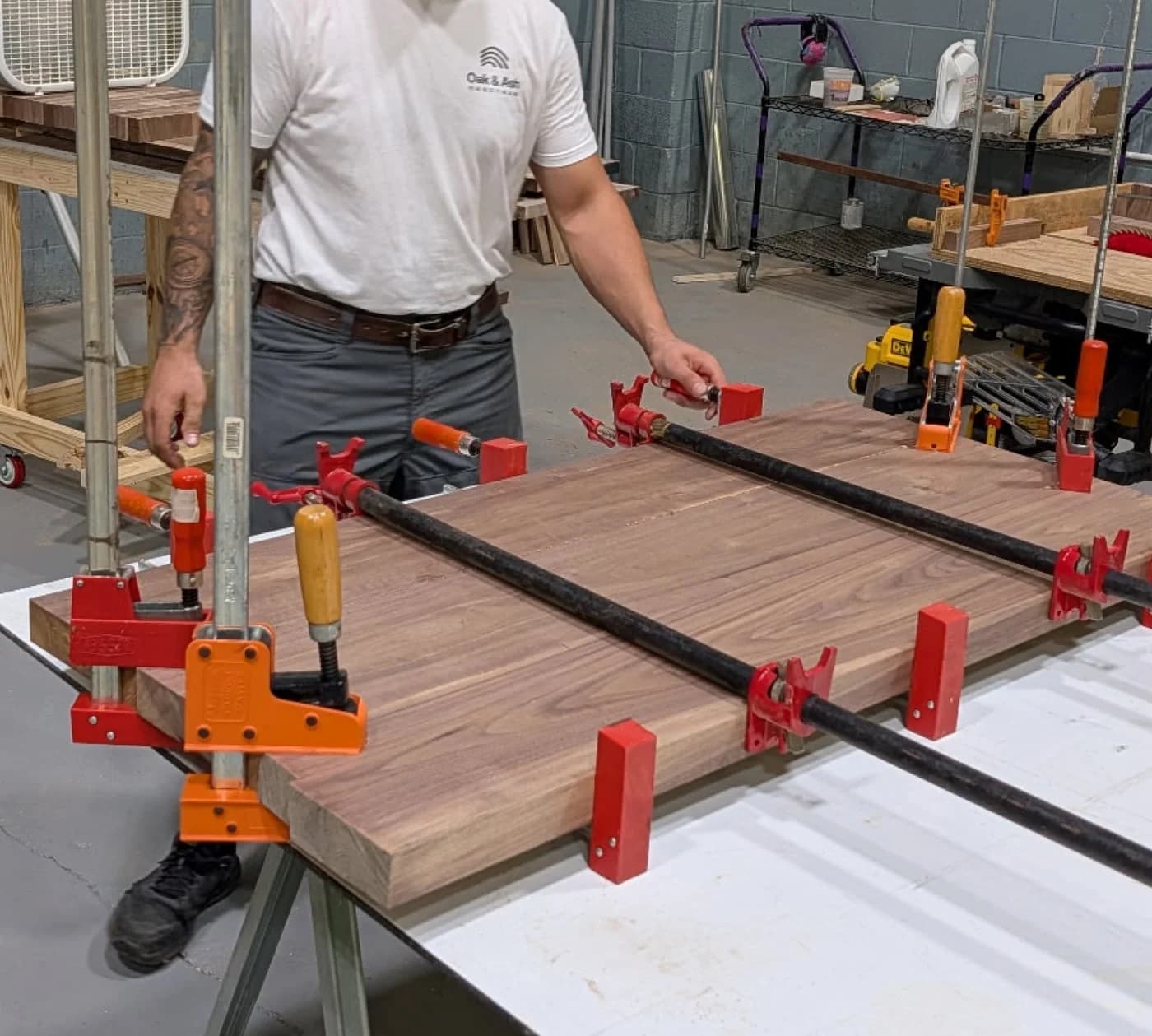 A maker clamping a hardwood tabletop across a workbench in the Oak & Ash shop.