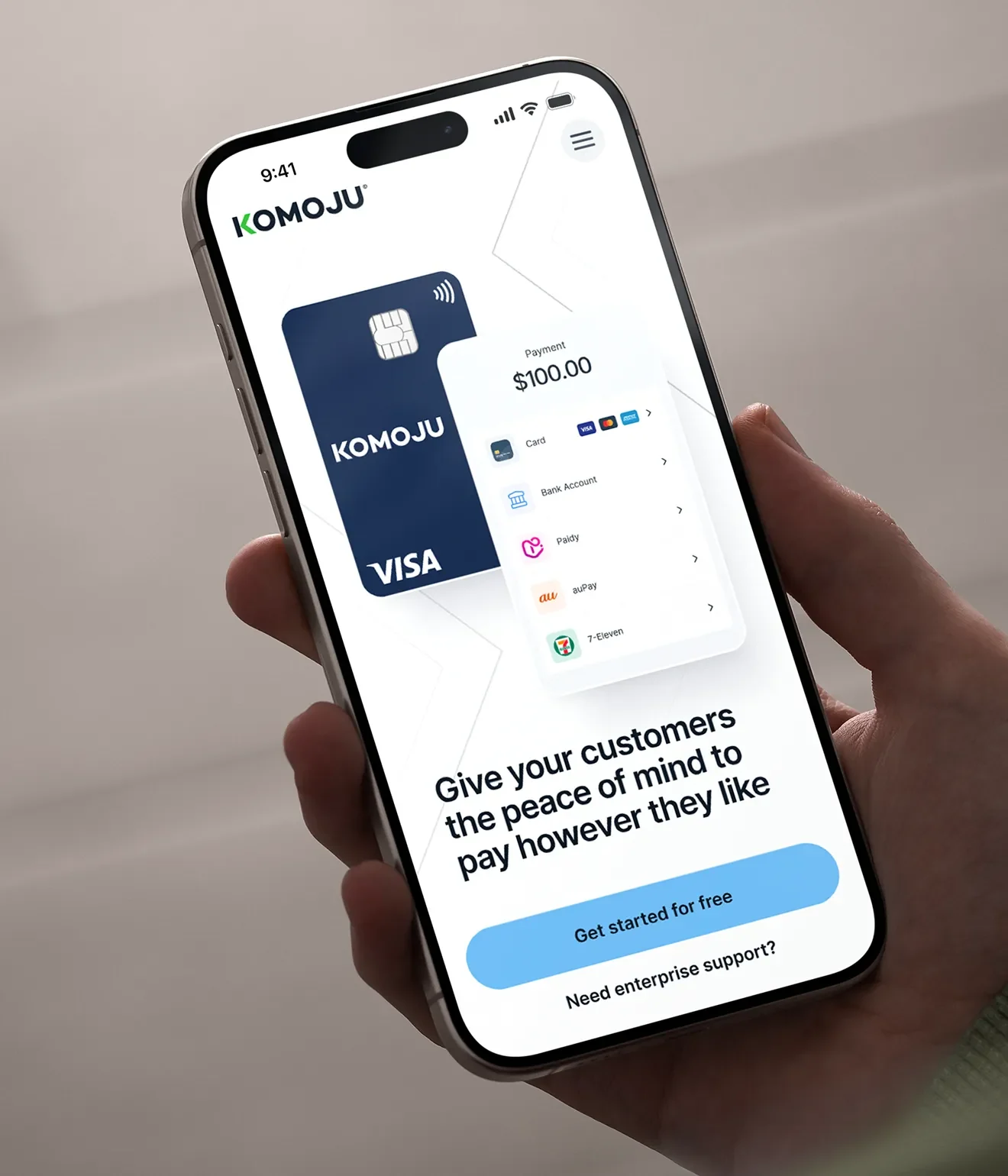 A hand holding a phone showing the KOMOJU payments app with a virtual Visa card.