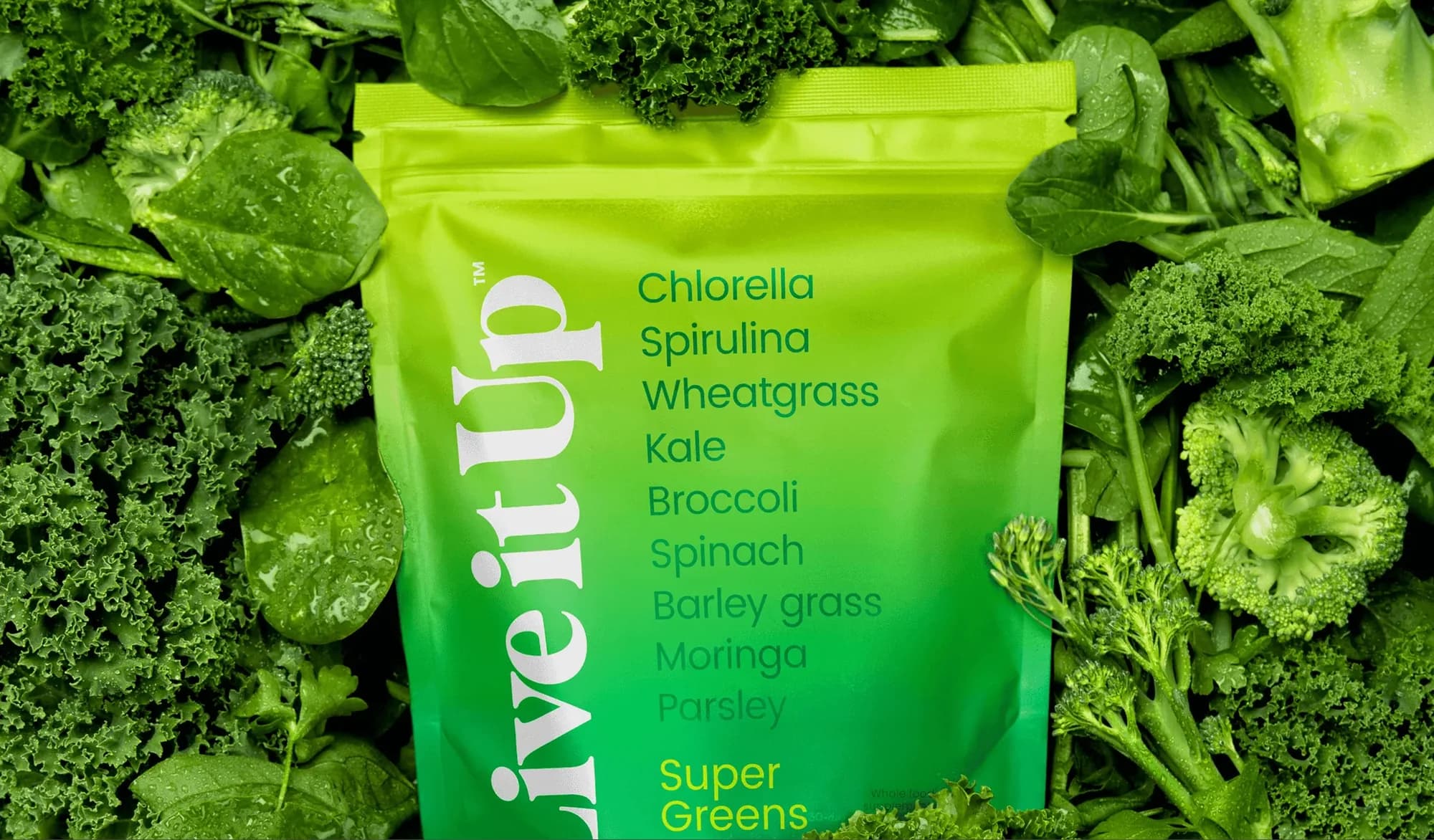 A bright green Live it Up Super Greens pouch photographed on a bed of kale, spinach and broccoli.